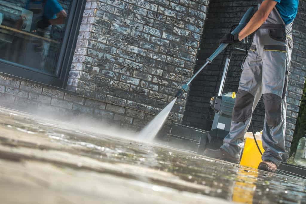Man power washing driveway illustrating exterior cleaning services in Pensacola, Florida.